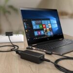 Open HP laptop on a wooden desk, powered by a large wall adapter and connected cables visible on the right.
