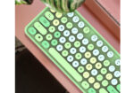 Pastel green rounded-key keyboard on a pink surface, seen at an angle with a plant above.